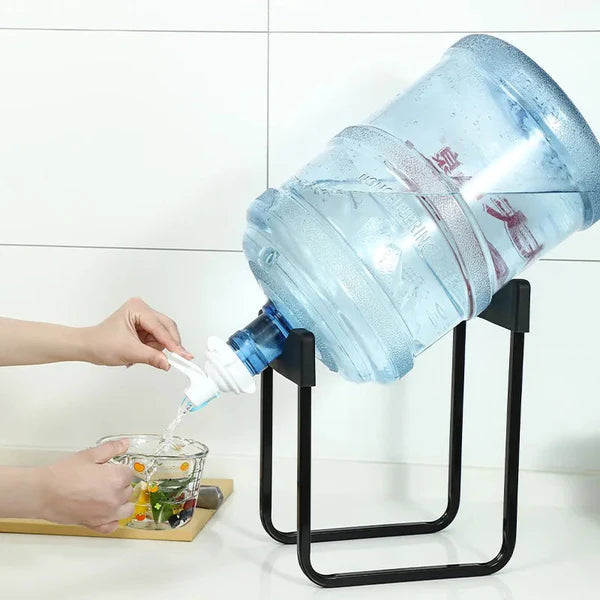 Person pouring water from a large water bottle into a glass using a black stand.