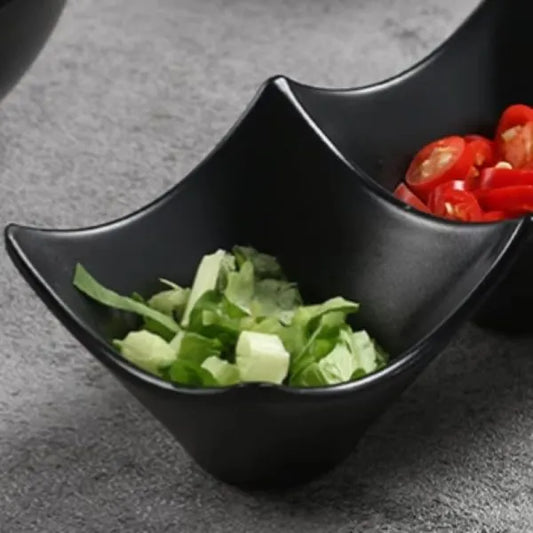 Black ceramic bowl with two compartments, one containing green salad and the other red cherry tomatoes, on a gray surface.