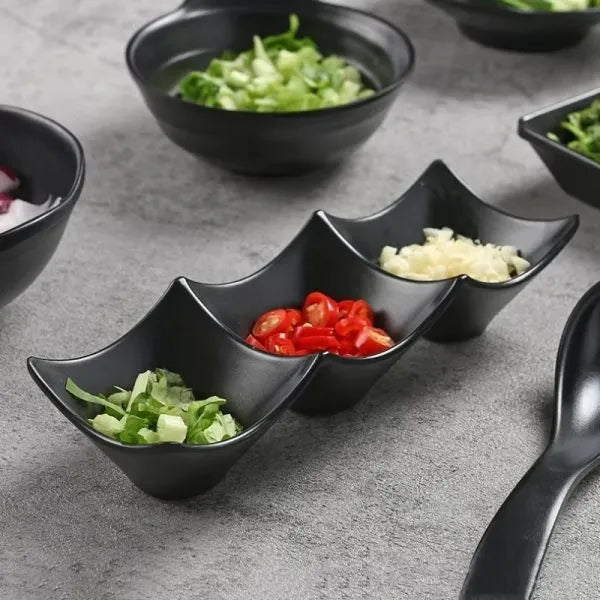 Black divided bowl with various ingredients on a gray surface