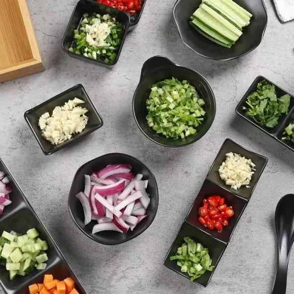 Assorted chopped vegetables in small black bowls on a gray surface