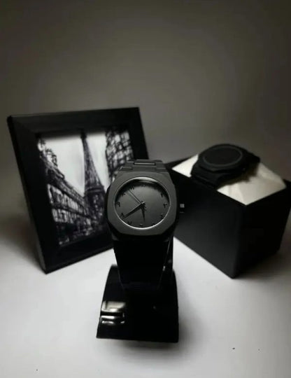 Black watch on a stand with a black box and photo frame in the background