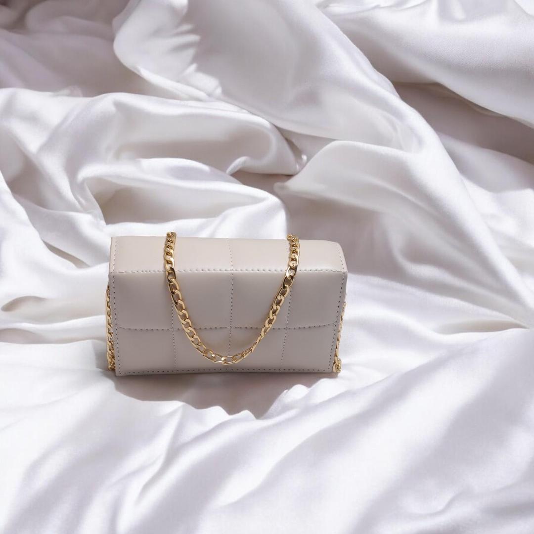 White handbag with a gold chain on a white fabric background