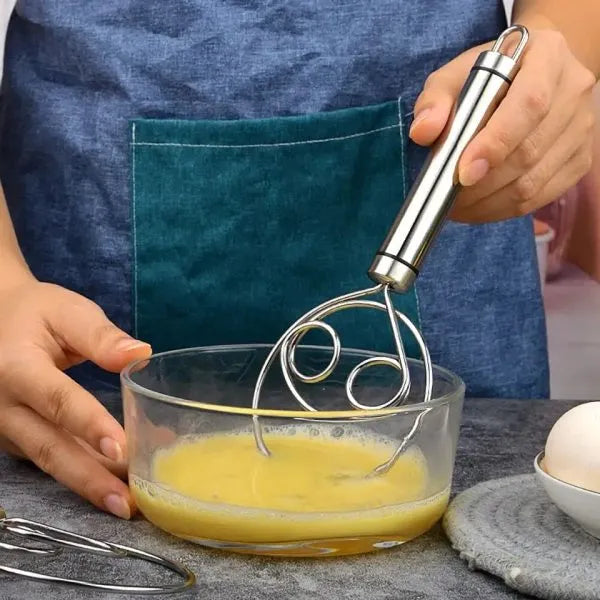 Person whisking eggs in a glass bowl with a metal whisk, wearing a blue apron.