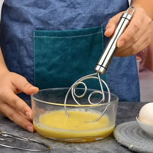 Person whisking eggs in a glass bowl with a metal whisk, wearing a blue apron.
