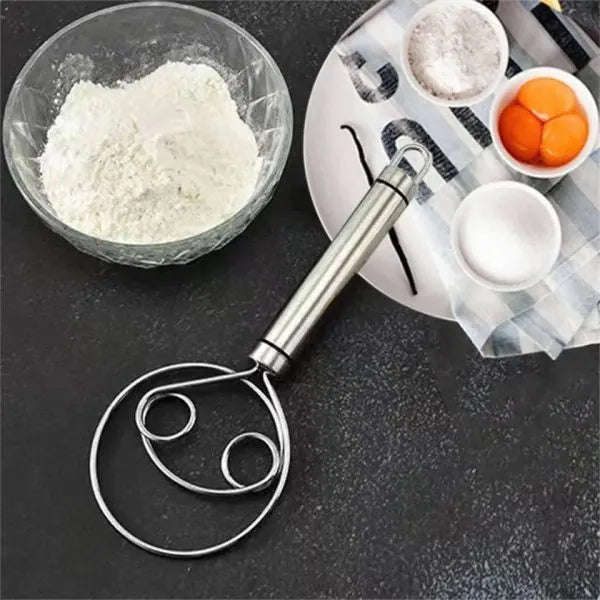 Metallic kitchen tool on a dark surface with flour and eggs in the background