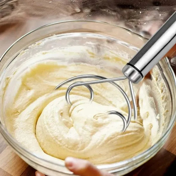 Hand mixer being used to whip cream in a glass bowl on a wooden surface