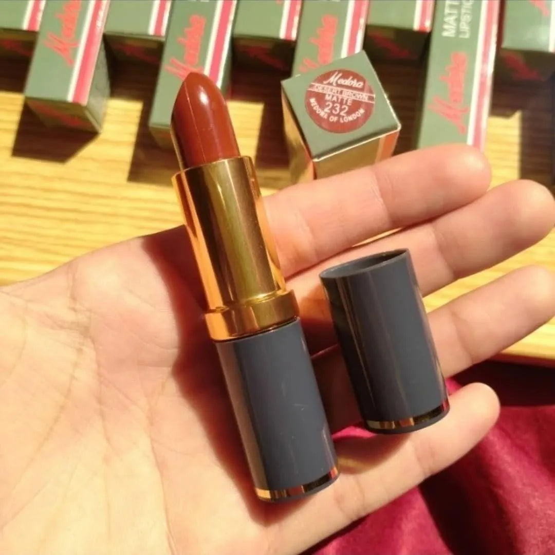 Lipstick with gold cap held in a hand, with red and green boxes in the background