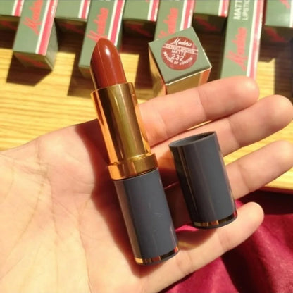 Lipstick held in a hand with product packaging in the background
