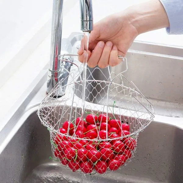 Person washing red berries in a wire basket under running water from a faucet.